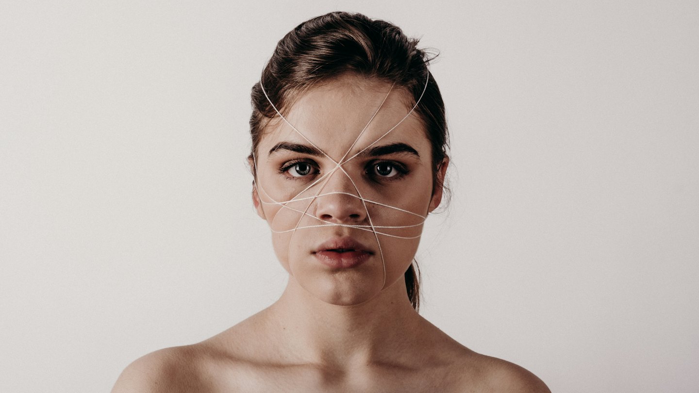 Volto di donna avvolto in sottili fili bianchi con capelli scuri raccolti.