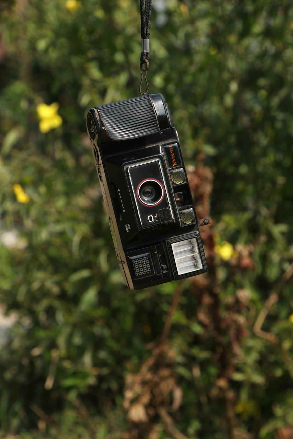 Una macchina fotografica a pellicola vintage appesa a una tracolla in un giardino.